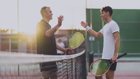 Handschlag von zwei Männern auf dem Tennisplatz mit Schlägern in der Hand