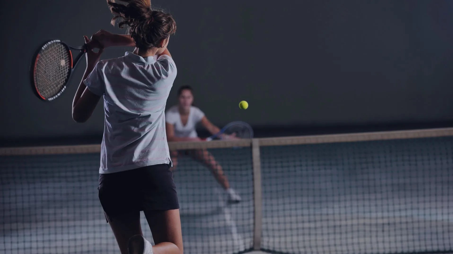 Tennisspielzweier Frauen in dunkler Tennishalle